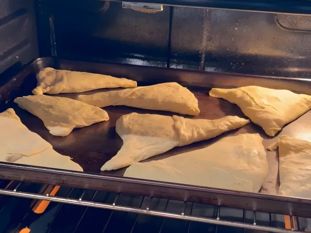 Raw byrek triangles on a baking sheet in the oven