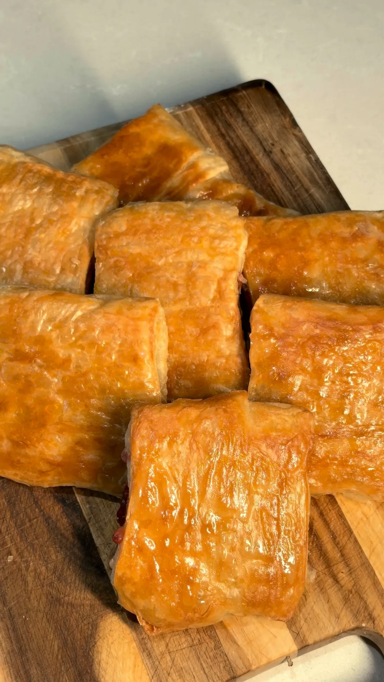Rolled byrek with pastry cream and strawberry jam, glossy and golden, on a wooden board