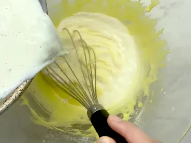 Hot milk pouring into whisked egg yolks in a glass bowl, a little at a time