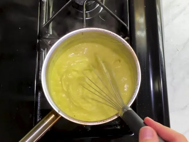 Thick yellow pastry cream in a saucepan on the stove, with the whisk leaving trails