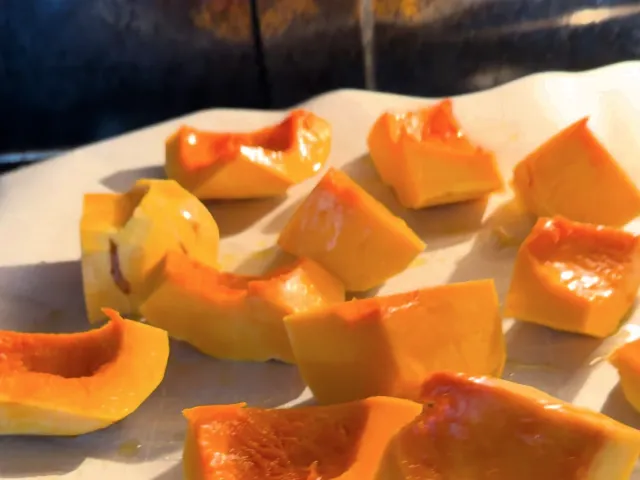 Peeled pumpkin pieces with a little olive oil on parchment paper, going into the oven