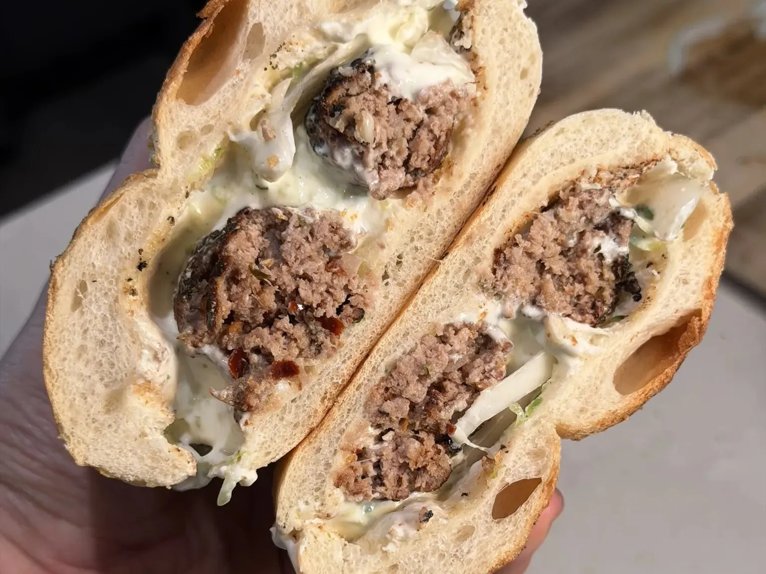 Bukë me qofte, a bread roll with grilled qofte, tzatziki and onions, cut in half and held in the hand