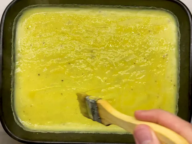 Brushing beaten egg over the vanilla custard in a dark baking tray