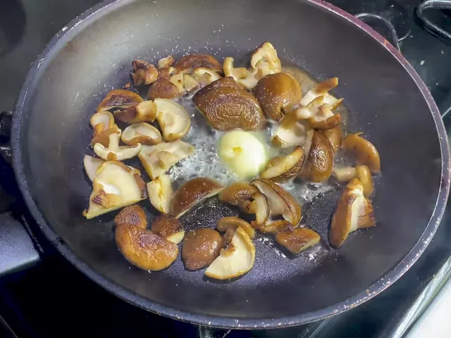 Browned shiitake pieces in a frying pan, with a pat of butter melting in the middle