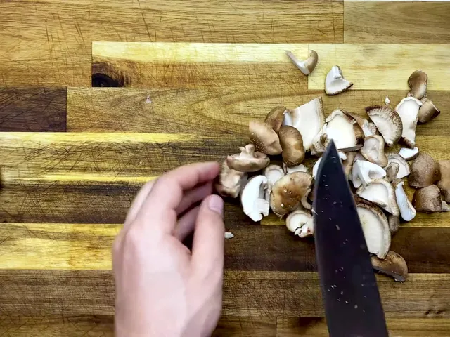 Shiitake mushrooms cut into halves and quarters on a wooden cutting board, with a chef’s knife