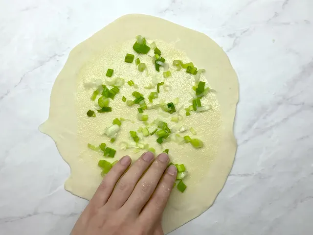 A thin round of dough brushed with olive oil in the middle, with salt and sliced scallions pressed on by hand