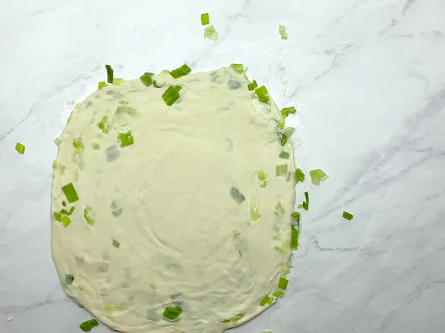 A coiled scallion pancake rolled flat again, with the spiral and bits of scallion showing through the dough