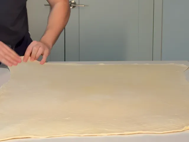 A sheet of byrek dough stretched thin across a whole kitchen island