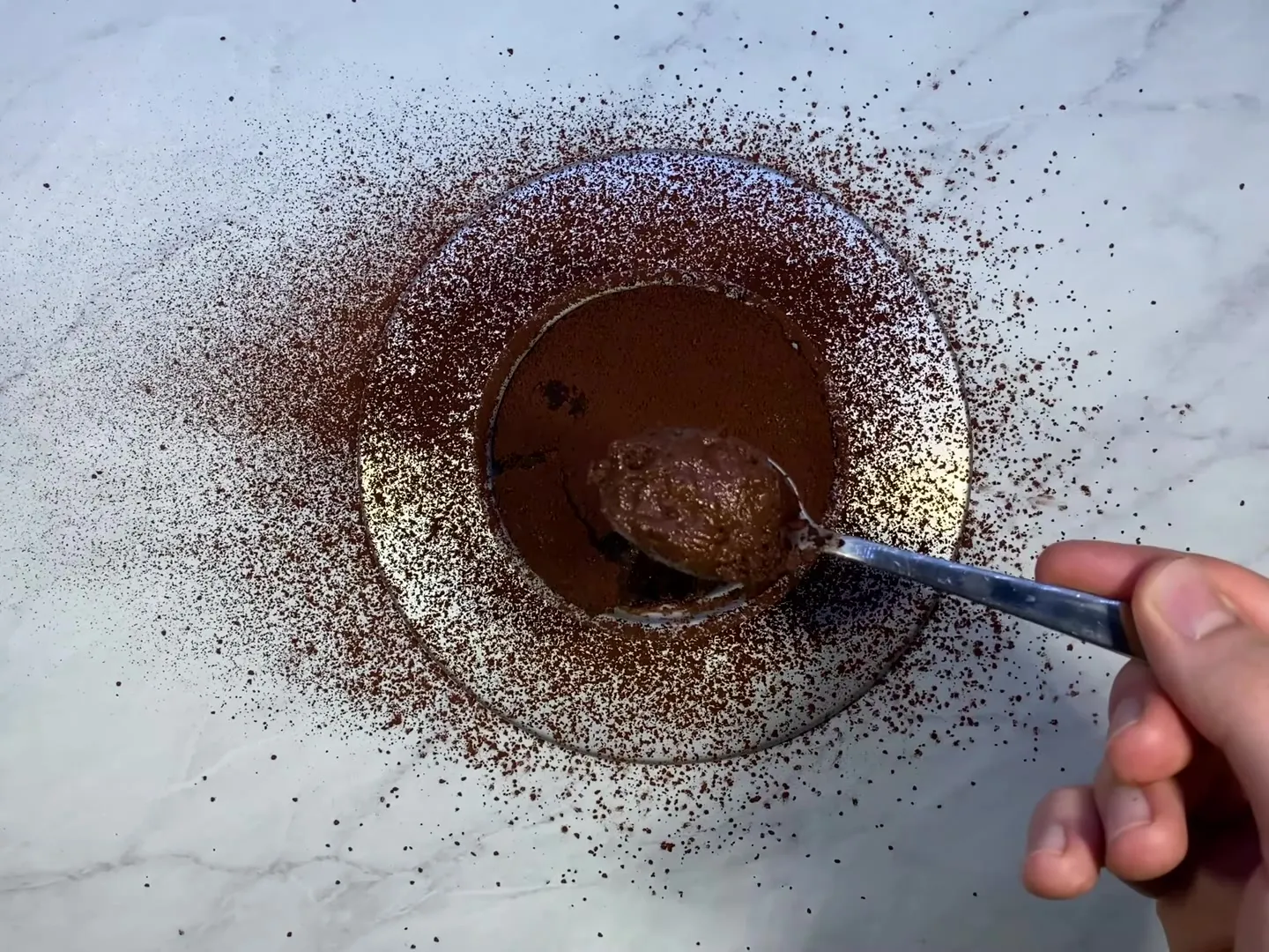 A spoonful of chocolate souffle lifted out of the ramekin, with cocoa powder dusted all around it