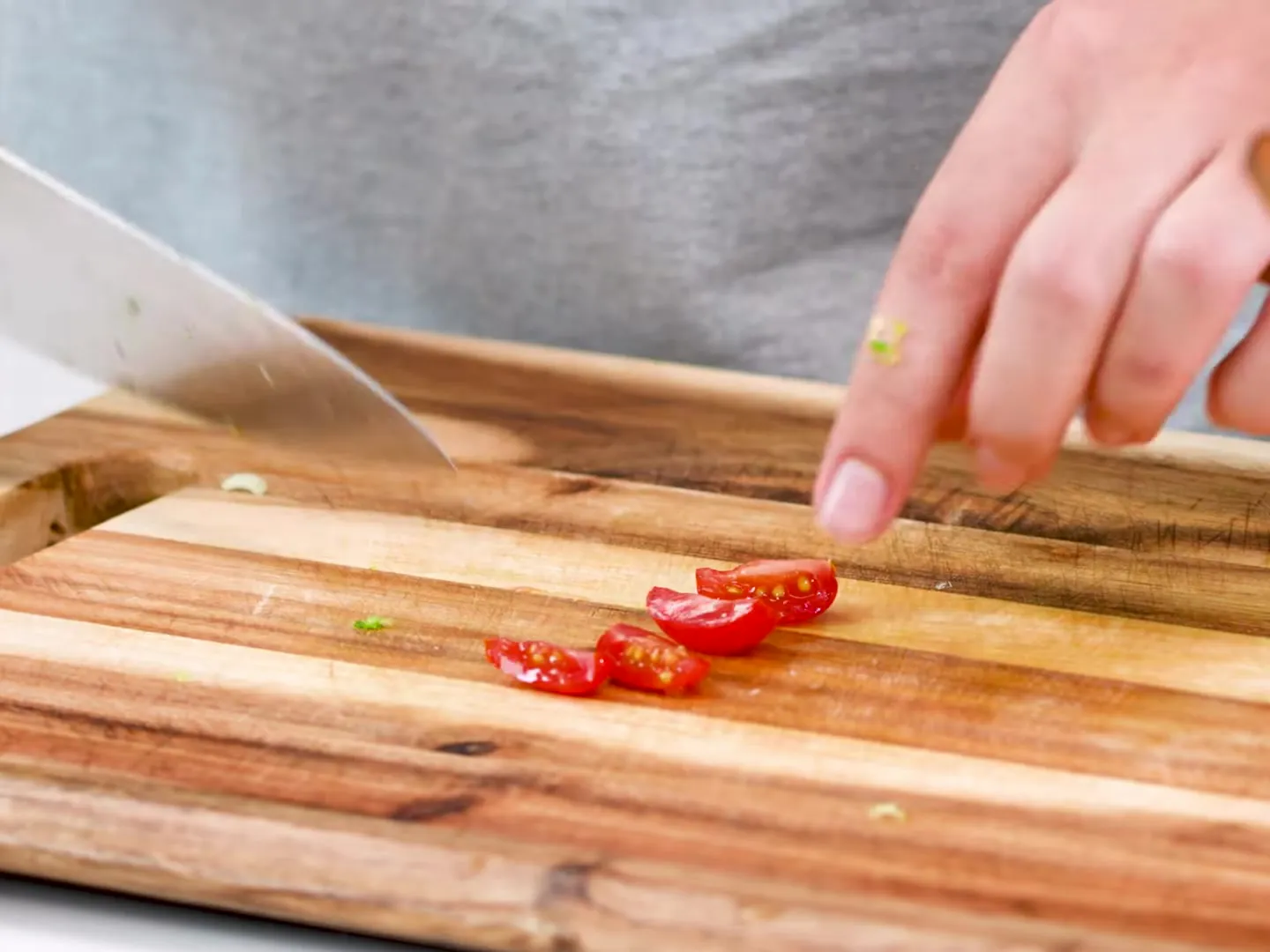 A cherry tomato cut into quarters on a wooden board, next to a chef’s knife