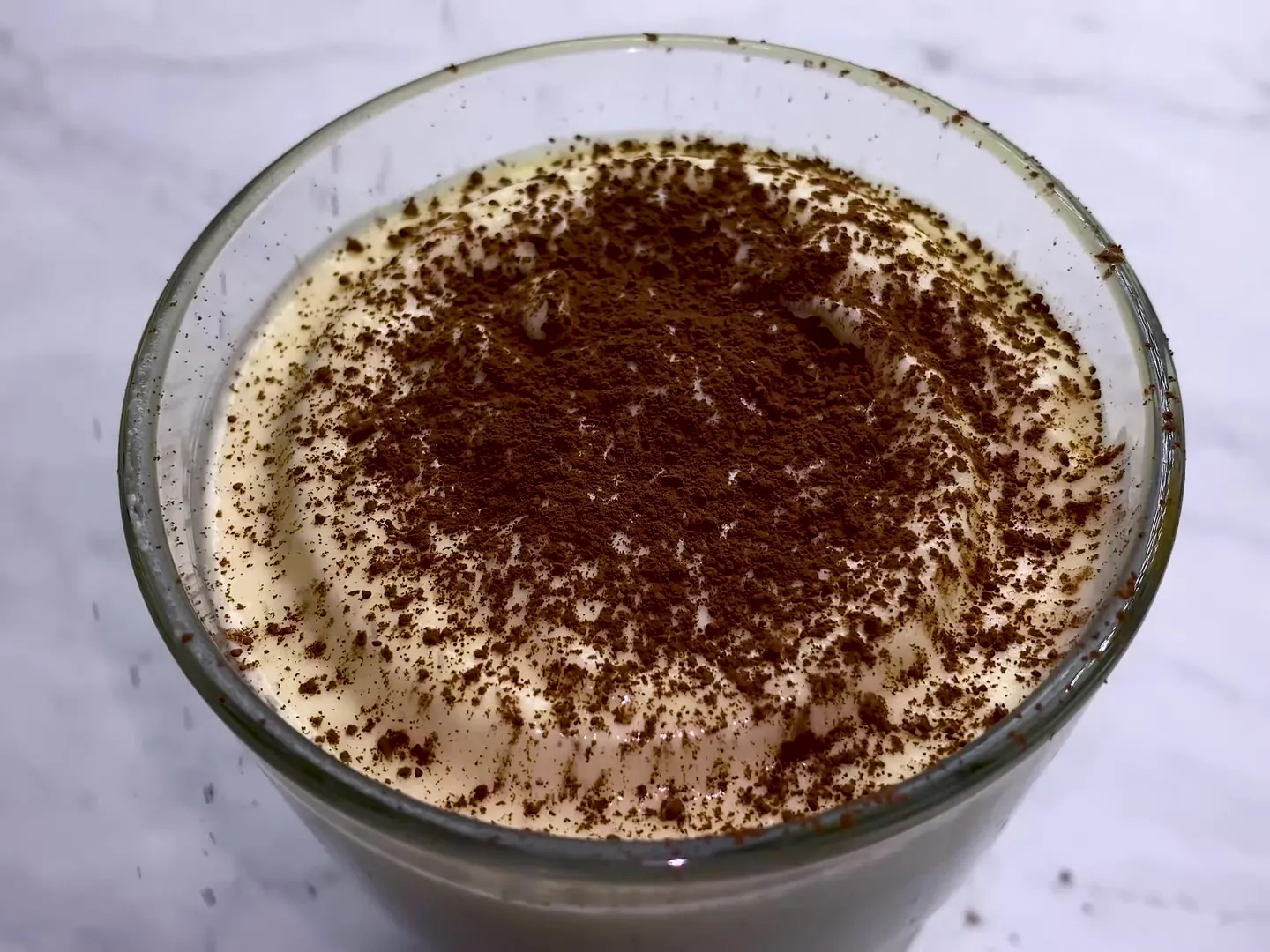 Cocoa powder dusted over the mascarpone cream in a glass of tiramisu, seen from above