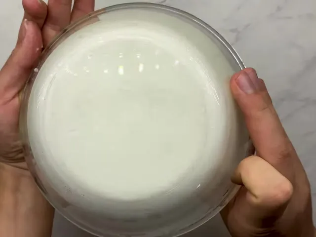 A glass bowl of whipped egg whites held upside down, the whites staying stuck to the bottom of the bowl