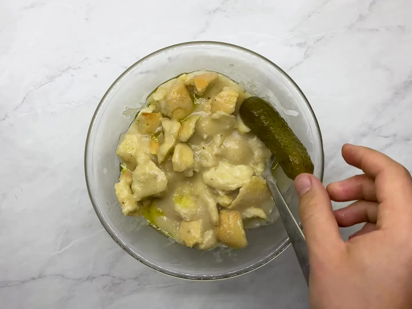 A glass bowl of trahana over bread with a spoon, and a pickle on the side of the bowl