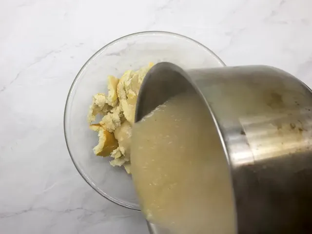 Thick trahana poured from a saucepan over broken bread in a glass bowl