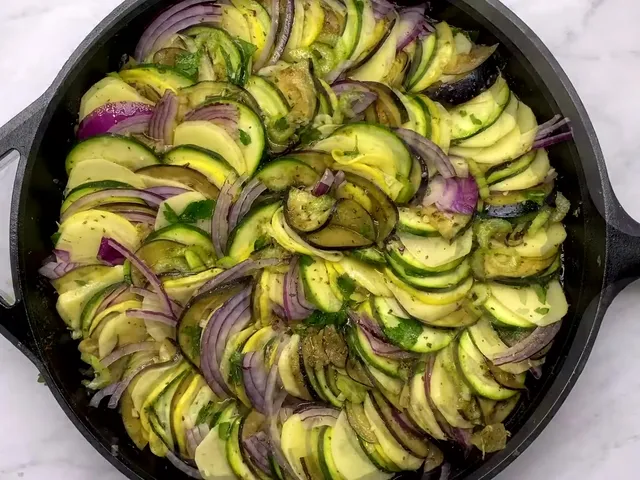 Raw slices of potato, zucchini, yellow squash, eggplant and red onion layered in a circle in a cast-iron skillet, ready for the oven