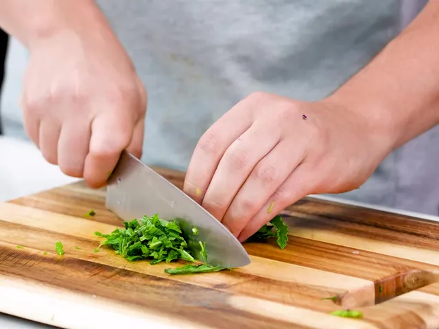 Hands slicing fresh mint leaves into thin strips with a chef's knife on a wooden board