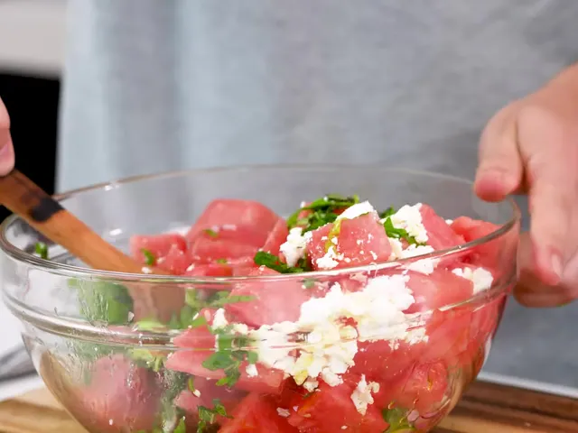 Mixing watermelon cubes, crumbled feta and herbs with a wooden spoon in a glass bowl