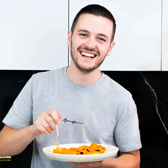Xhulio laughing in his kitchen with a plate of pasta